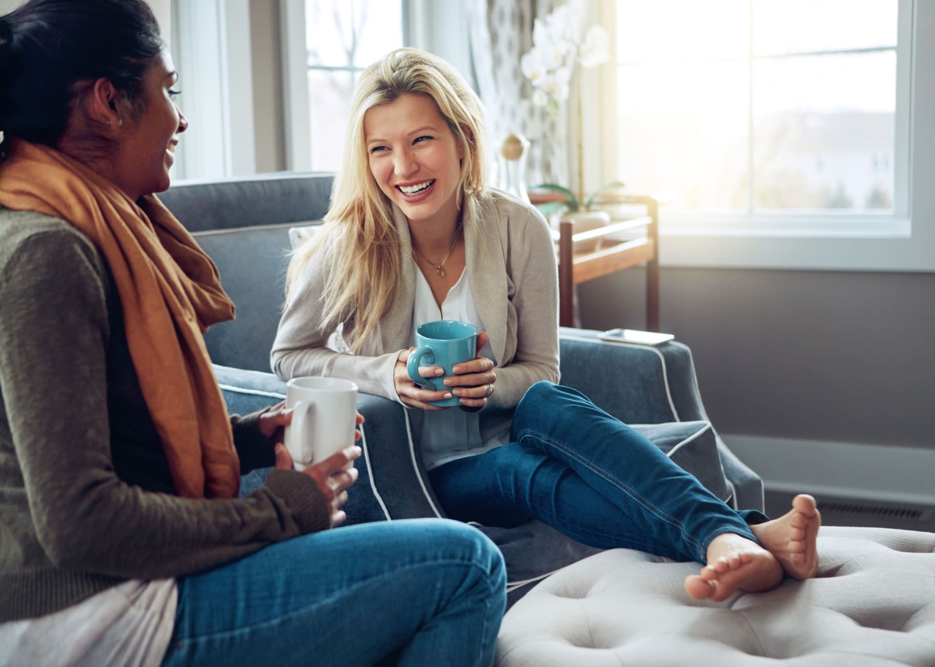 Two smiling women sat down with coffee laughing